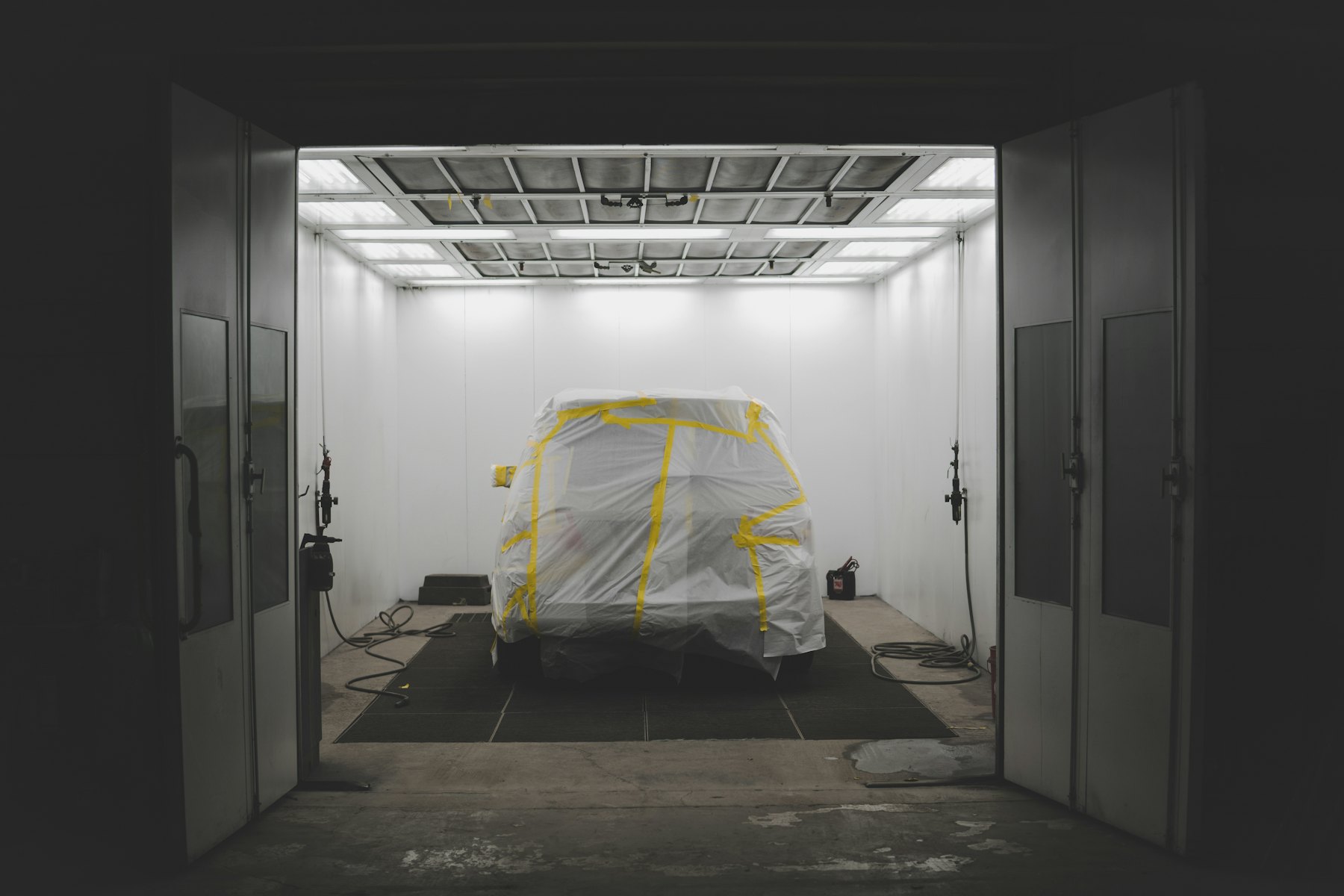 A car masked and taped inside a lit paint booth