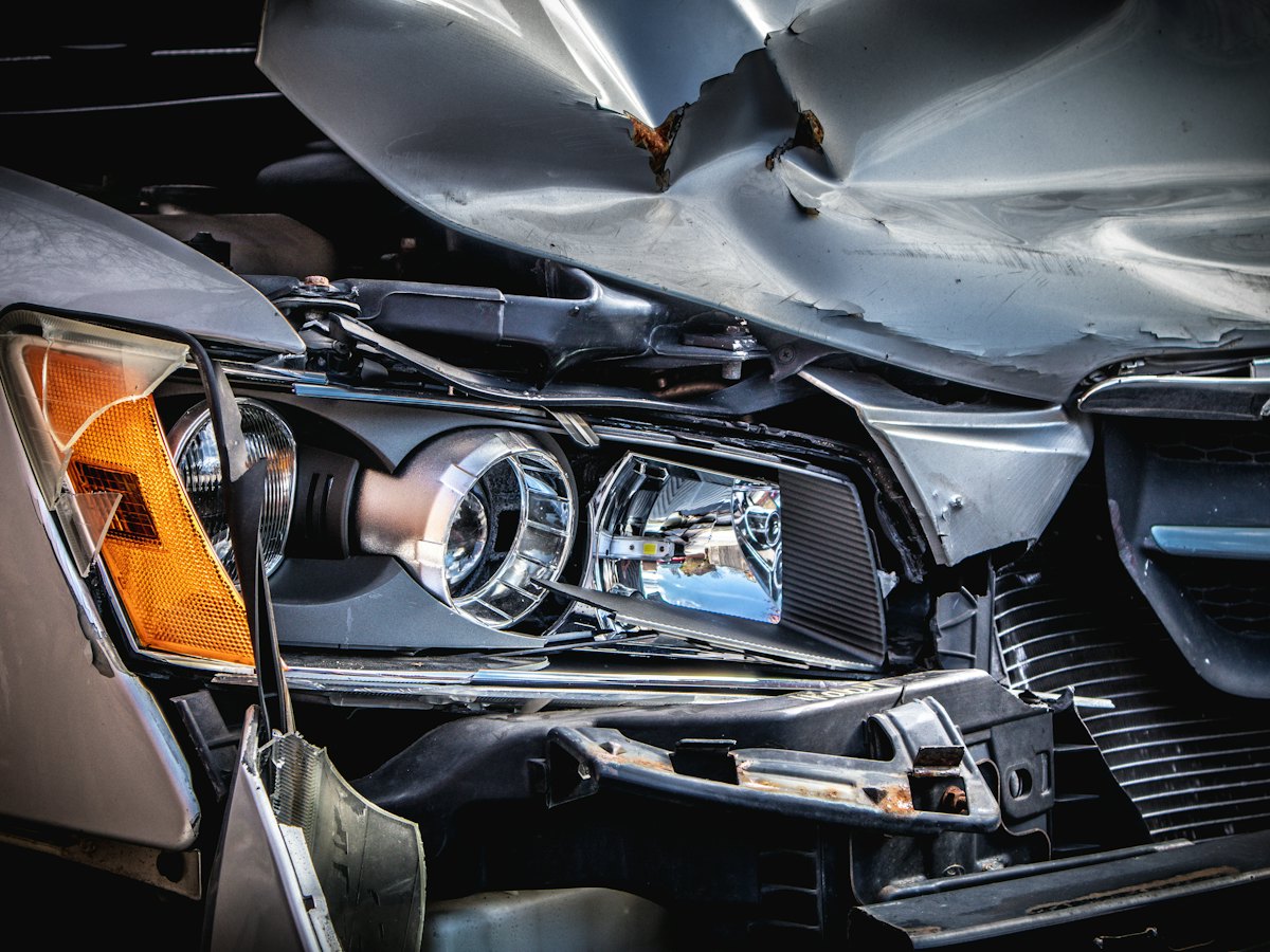 Front end of a silver car with a crushed hood and broken headlight
