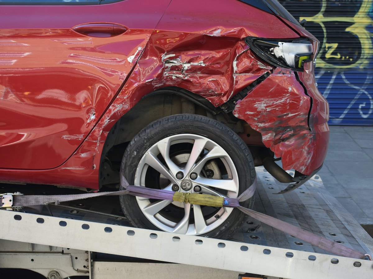 A red car with side damage strapped to a flatbed tow truck