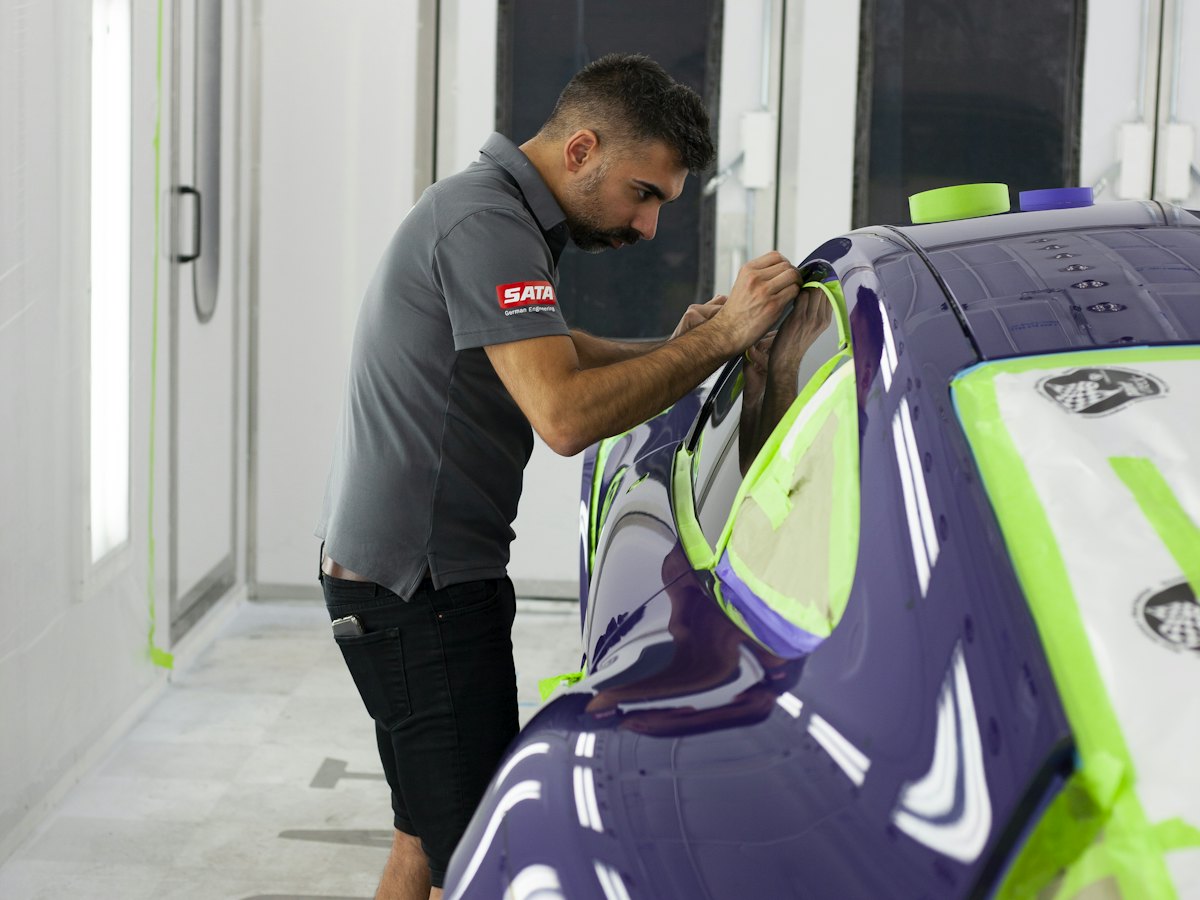 Technician masking a car for paint inside a spray booth